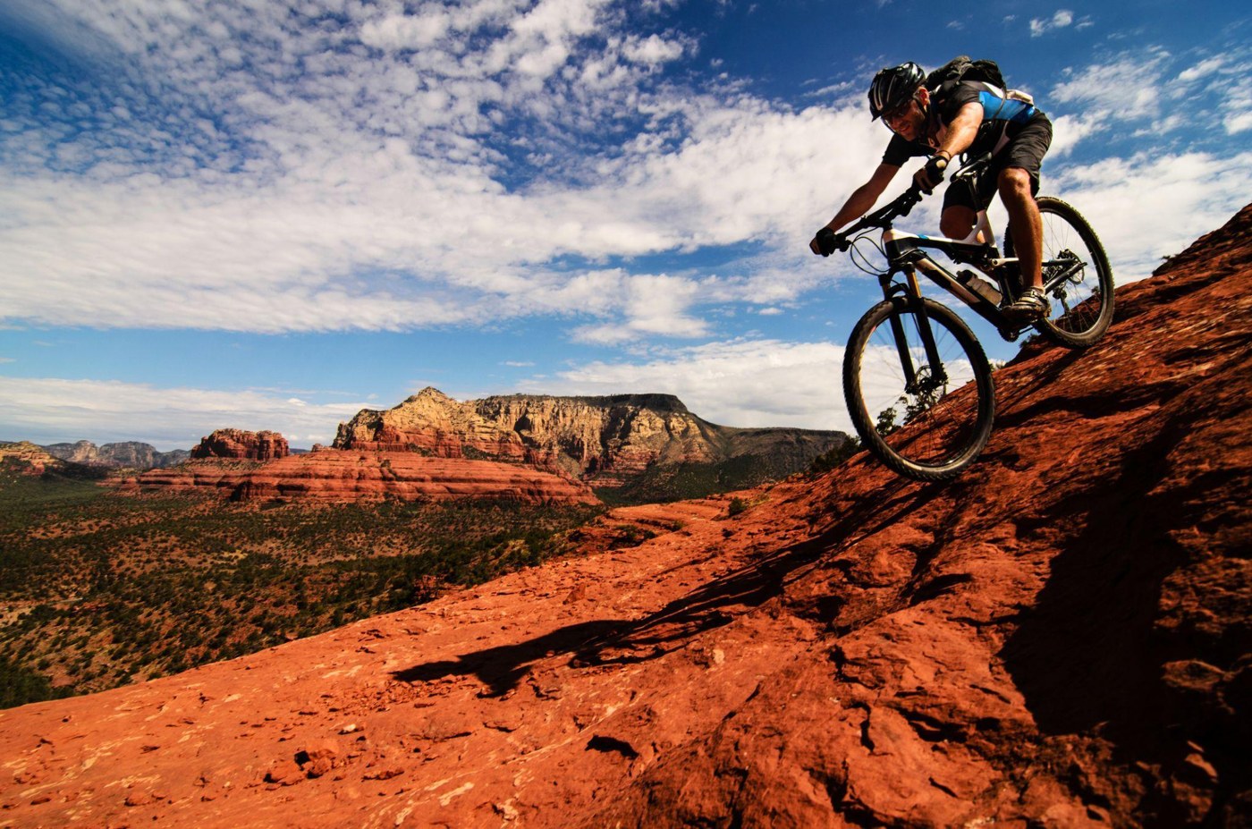 A mountain biker riding across red rock with a desert landscape beyond