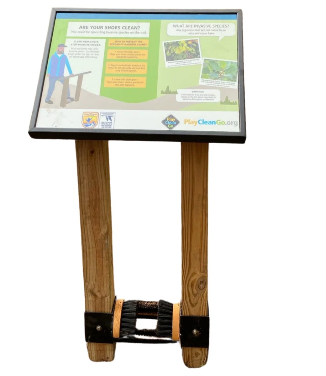 A PlayCleanGo interpretive sign mounted above a boot brush